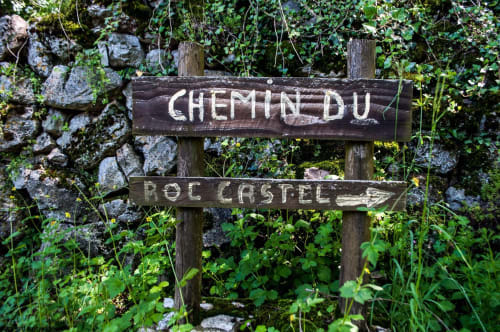 Wooden trail sign for Chemin du Roc Castel at Hôtel Du Rocher in Le Caylar, France