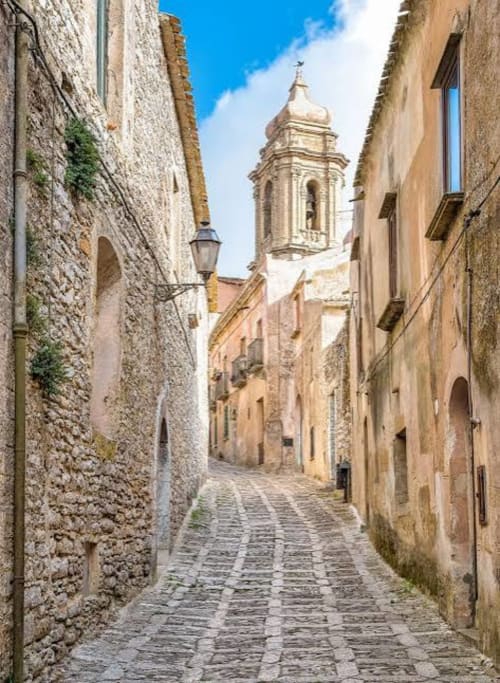 Strettissima via in ciottoli a Marausa con edifici storici in pietra e campanile della chiesa, Villa Giulia sul Mare