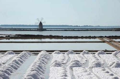 Saline con mucchi di sale bianco e mulino a vento a Marausa Lido, Sicilia, vicino a Villa Giulia sul Mare