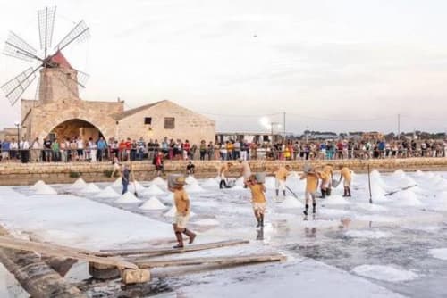 Tradizionali vasche di sale a Marausa lido, Sicilia con mulino storico e operai che raccolgono sale marino