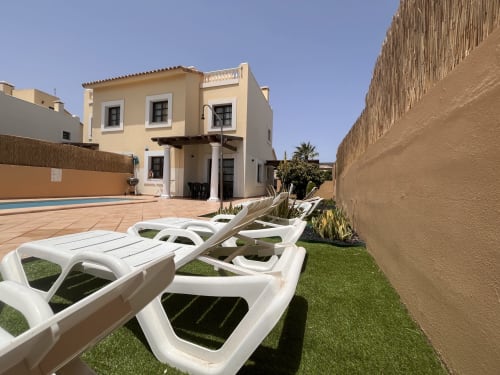 Cream villa with white lounge chairs on artificial grass, pool and terrace in Geafond, Spain