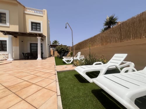Villa patio with white loungers, terracotta tiles, manicured lawn, and ocean views at FTV Holidays Homes Casa Reguera in