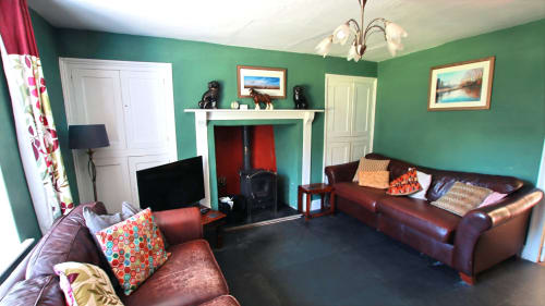Spacious villa living room in Llandysul with green walls, burgundy leather sofas, fireplace, TV, and modern furnishings