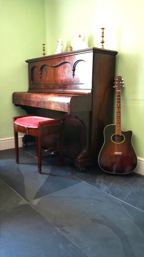 Wooden piano with red bench and acoustic guitar in green-walled music room at Llwyncadfor holiday home, Llandysul