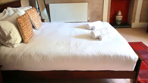 Luxurious bedroom at Llwyncadfor villa in Llandysul with white linens, orange patterned pillows, rolled towels, and radiator