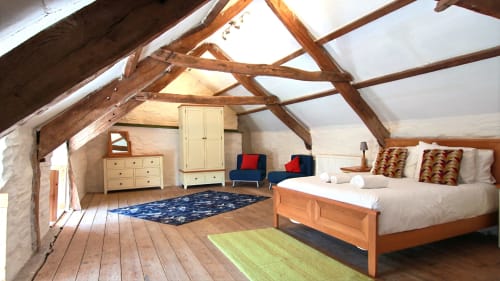 Spacious attic bedroom at Llwyncadfor villa with exposed beams, wooden bed, white linens, and colorful cushions in Llandysul.