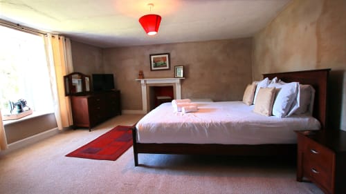 Spacious master bedroom in Llwyncadfor villa with queen bed, fireplace, and red pendant light in Llandysul