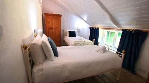 Cozy attic bedroom at Llwyncadfor holiday home in Llandysul with white bedding, wooden beams, and dark curtains