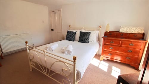 Spacious bedroom at Llwyncadfor villa in Llandysul with cream metal bed frame, black cushions, wooden dresser, and natural