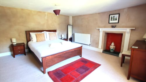 Spacious villa bedroom at Llwyncadfor with wooden bed, fireplace, red rug, and period furnishings