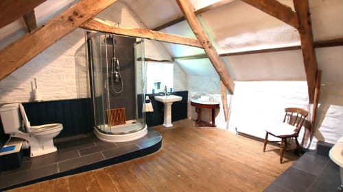 Spacious attic bathroom in Llandysul villa with shower enclosure, toilet, pedestal sink, wooden beams, and rustic charm
