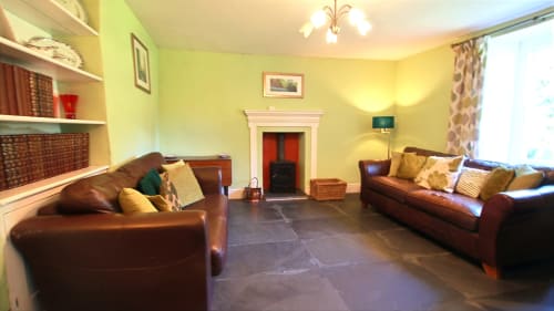 Bright yellow living room at Llwyncadfor villa in Llandysul with two brown leather sofas, fireplace, and slate flooring