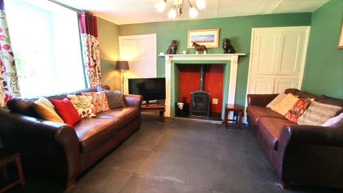 Spacious green living room with leather sofas, fireplace, TV, and colorful cushions at Llwyncadfor holiday home in Llandysul