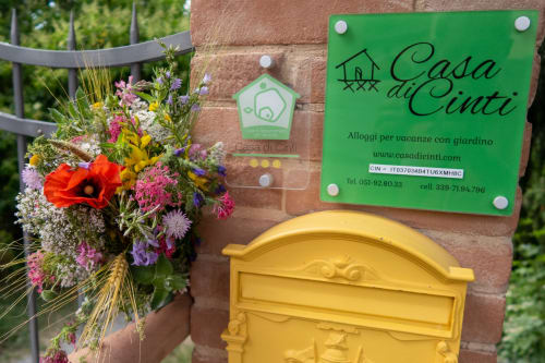 Ingresso della Casa di Cinti a Loiano con fiori colorati, insegna verde e cassetta postale gialla