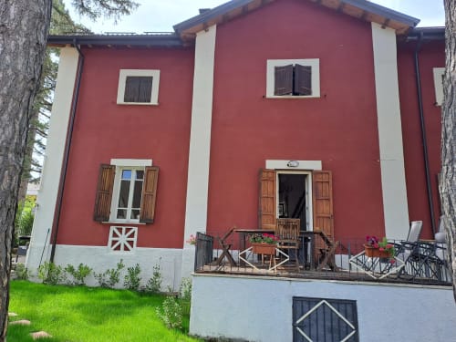 Villa Antico Chalet Momosa a Ovindoli con muri rossi, cornici bianche, persiane in legno e vista montagna dalla terrazza