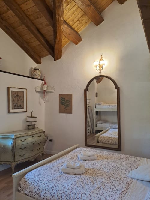 Camera da letto rustica all'Antico Chalet Momosa con travi in legno a vista, specchio arcuato, cassettone vintage e biancheria floreale