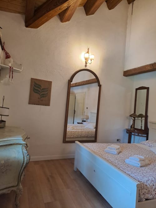 Camera da letto rustica nella villa Antico Chalet Momosa, Ovindoli, con travi in legno, specchio ad arco, letto bianco e arredamento tradizionale