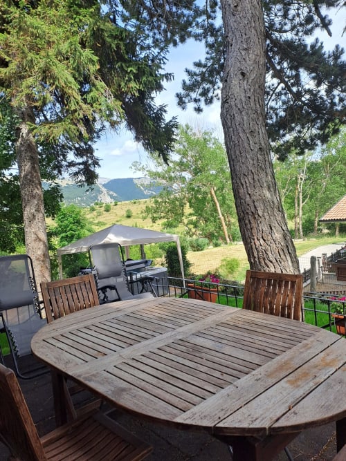 Tavolo da pranzo in legno sulla terrazza dell'Antico Chalet Momosa di Ovindoli, con vista sulle montagne e alti pini