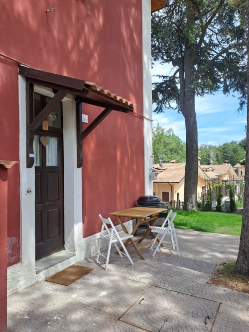 Patio della villa rossa con tavolo in legno e sedie bianche presso l'Antico Chalet Momosa, montagne di Ovindoli