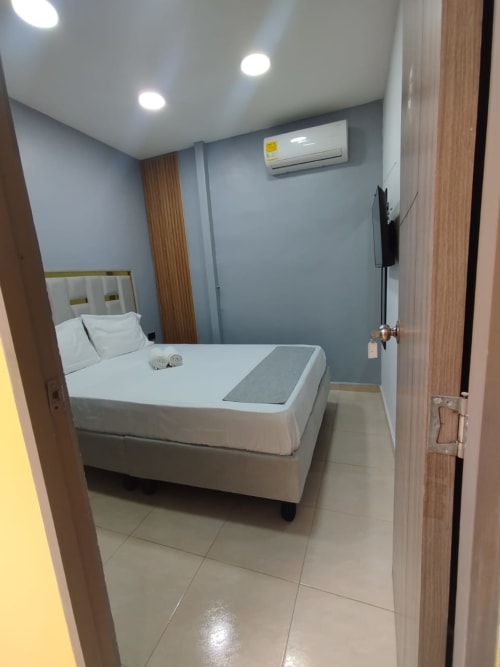 Habitación moderna con cama doble en Hotel Casa Mango en Cali, con ropa de cama blanca, aire acondicionado, TV y piso de cerámica