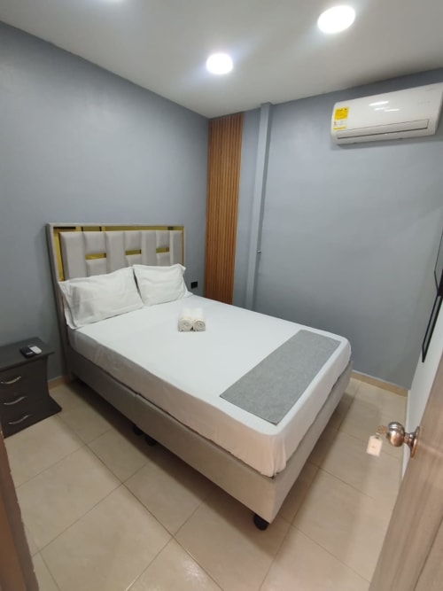 Habitación moderna en hotel CASA MANGO en Cali con cama queen, sábanas blancas, paredes grises y aire acondicionado