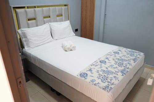 Cama doble moderna en hotel Casa Mango de Cali con sábanas blancas, toallas enrolladas y manta azul estampada