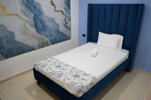 Moderno dormitorio en Casa Mango, Cali con cama doble, cabecero azul, sábanas blancas y obra de arte abstracta azul en la pared
