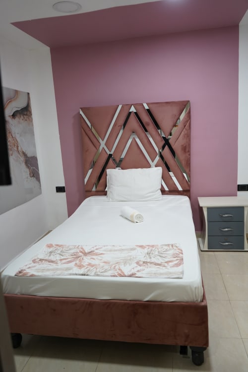Moderno dormitorio del hotel Casa Mango en Cali con pared de acento rosa, cabecero geométrico, ropa de cama blanca y detalles oscuros