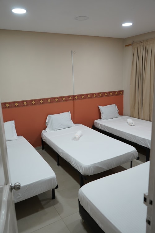 Tres camas individuales con ropa blanca y cabeceros naranjas en una habitación del hotel Casa Mango, Cali con cortinas beige