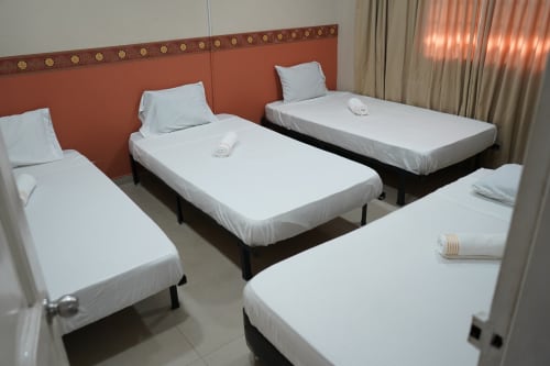 Habitación del hotel Casa Mango en Cali con cuatro camas individuales, sábanas blancas, cabecero naranja y ventana con cortinas