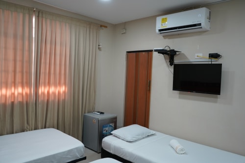 Moderno cuarto de hotel en Casa Mango Cali con camas gemelas, TV de pared, aire acondicionado y cortinas beige al atardecer