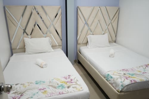 Dos camas gemelas con cabeceras geométricas beige y sábanas blancas en el hotel Casa Mango de Cali, Colombia