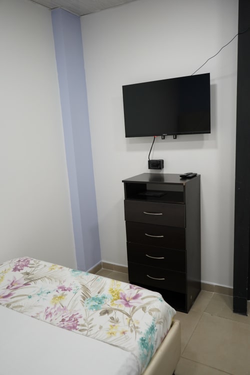 Moderna habitación del hotel Casa Mango en Cali con ropa de cama floral, mueble TV negro, televisor plano montado en pared y acento azul