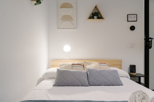 Habitación moderna en Stay Gest Valencia con cabecero de madera, almohadas acolchadas, ropa de cama blanca, cuadros decorativos e iluminación ambiental