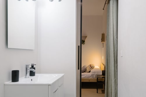Baño de Stay Gest Valencia con lavabo blanco, grifo moderno y vista al dormitorio con iluminación cálida