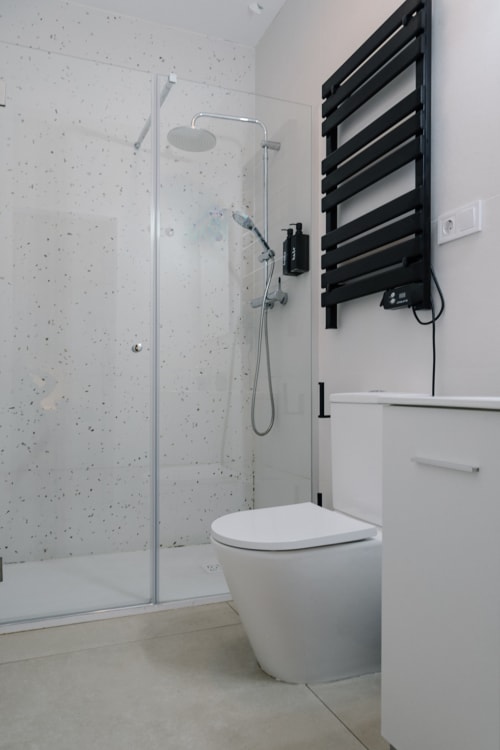 Baño moderno en Stay Gest Valencia con ducha abierta, inodoro, toallero negro y paredes estilo terrazo