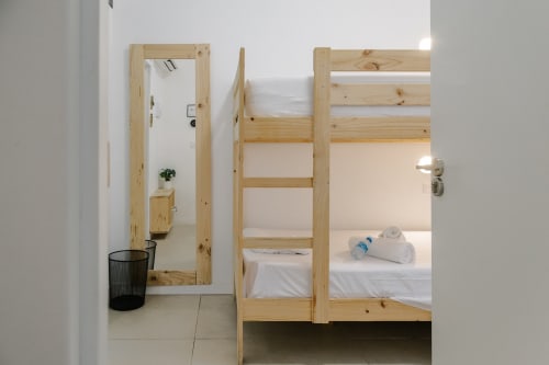 Literas de madera modernas con sábanas blancas en habitación del hostal Stay Gest, Valencia, con espejo y acceso al baño