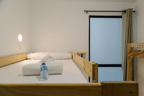 Habitación limpia con cama de madera, ropa blanca, toallas enrolladas y botella de agua en el hotel Stay Gest Valencia