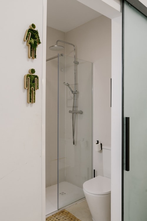 Baño moderno con ducha de efecto lluvia, inodoro y muro de arte musgo en el hotel Stay Gest Valencia