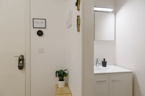 Baño moderno en Stay Gest Valencia con mueble blanco, espejo, lavamanos y planta en maceta sobre estante de madera