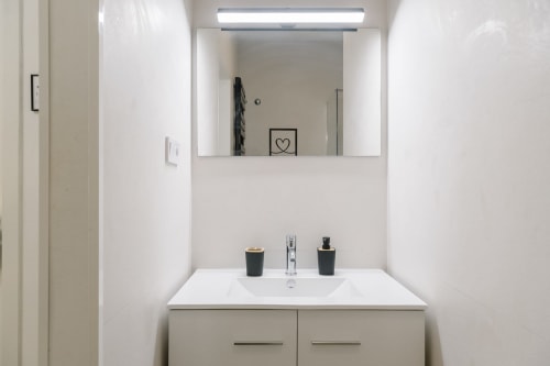 Baño moderno en Stay Gest Valencia con vanidad blanca, espejo iluminado y accesorios cromados en la habitación Niña Mala 2