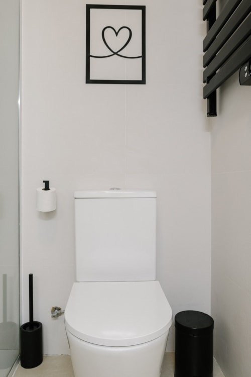 Baño moderno con inodoro blanco, accesorios negros y decoración con corazones en el hotel Stay Gest de Valencia