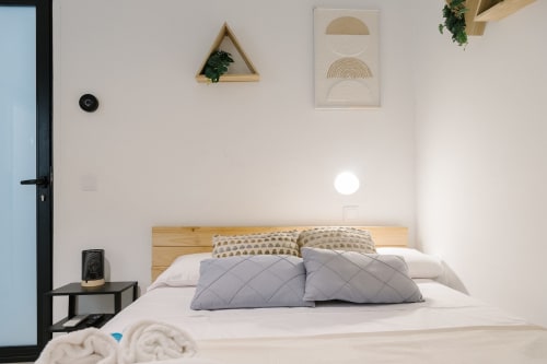 Dormitorio moderno en Stay Gest Valencia con cama de madera, almohadas grises, ropa de cama blanca, arte mural y decoración minimalista