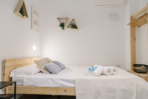 Dormitorio luminoso en Stay Gest Valencia con cama de madera, ropa de cama blanca, almohadas azules, plantas murales y comodidades modernas