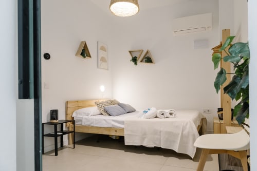 Luminoso dormitorio moderno en Stay Gest Valencia con cama de madera, ropa blanca impecable, plantas y mobiliario contemporáneo