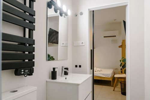 Baño moderno de Stay Gest Valencia con tocador blanco, toallero térmico negro, espejo y vista al dormitorio