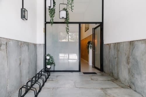 Recepción moderna de Stay Gest Valencia con paredes de hormigón, puertas de cristal y plantas colgantes que conducen a un interior luminoso