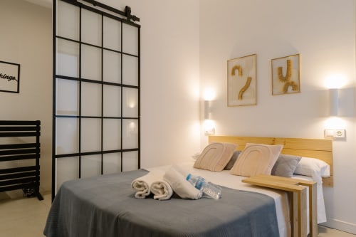 Dormitorio accesible y moderno en Stay Gest Valencia con cama de madera, toallas enrolladas, biombo de rejilla negra y decoración contemporánea