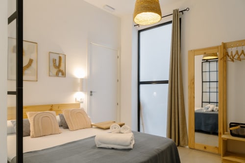 Dormitorio accesible en Stay Gest Valencia con cama de madera, ropa de cama gris, almohadas a rayas y abundante luz natural