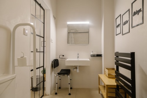 Baño accesible en Stay Gest Valencia con ducha a ras de suelo, lavabo mural, barras de apoyo y ayudas de movilidad